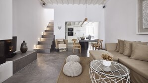 A modern living room with a sofa, ottomans, a coffee table, and a TV. - Crystal Green Signature Suites Mykonos (Mykonos)