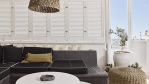 A modern living room with a black sofa, a white coffee table, and a large potted plant. - Crystal Green Signature Suites Mykonos (Mykonos)