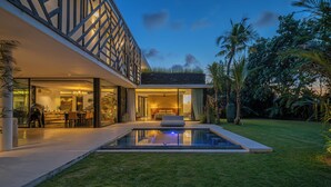 Una casa moderna amb un porxo de vidre, una piscina i vegetació exuberant.