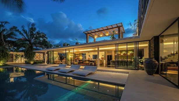 Una casa moderna amb piscina, parets de vidre i mobiliari exterior.