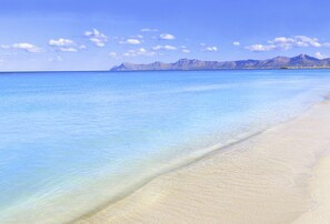Une plage à l’eau d’un bleu cristallin, avec une chaîne de montagnes en arrière-plan.