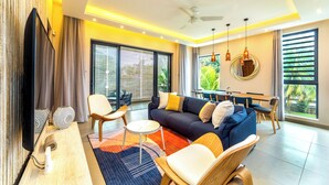 Ein modernes Wohnzimmer mit Sofa, Sesseln, einem Esstisch und einem Fernseher.
