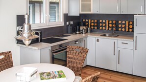 Une cuisine moderne avec des meubles gris, un pare-feu noir et un coin repas doté de chaises en osier.