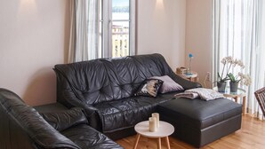 Un salon moderne avec un canapé en cuir noir, une petite table ronde sur laquelle se trouve une lampe, et un pot d’orchidée.