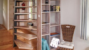 Une pièce avec une bibliothèque en bois, une chaise en osier et un extincteur posé sur le sol.