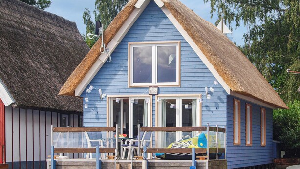 Une maison bleue avec un toit de chaume, une jetée en bois et une pancarte indiquant l’année 2003.