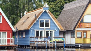 Une maison bleue avec un toit de chaume et une jetée qui s’avance dans l’eau.