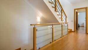 Un escalier moderne avec des marches en bois et des rampes en verre, menant à l’étage supérieur.