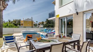 Un espace extérieur avec une piscine, des chaises longues, une table à manger agrémentée de sets de table et d’un centre de table, ainsi qu’un bâtiment doté d’un balcon et de grandes fenêtres.
