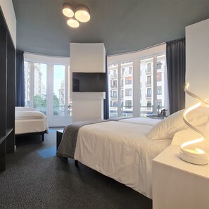 Habitació d'hotel moderna amb un llit gran, un televisor fixat a la paret i vistes a la ciutat a través de grans finestres.
