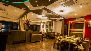 A restaurant with a marble floor, wooden furniture, and a red accent wall. - Hotel Prabha Palace (Ahmednagar)