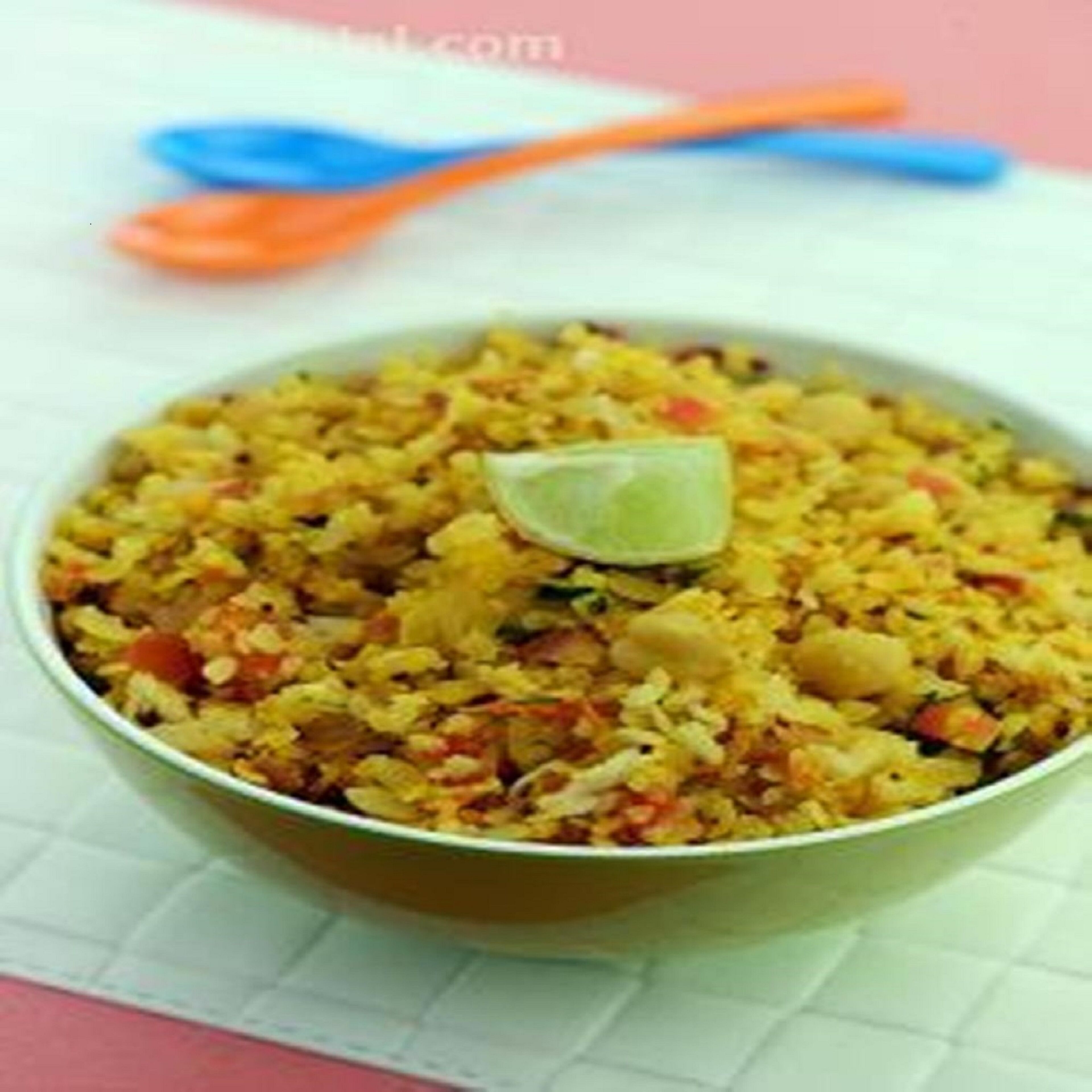 Un plato blanco con arroz amarillo, verduras y una cuña de lima.