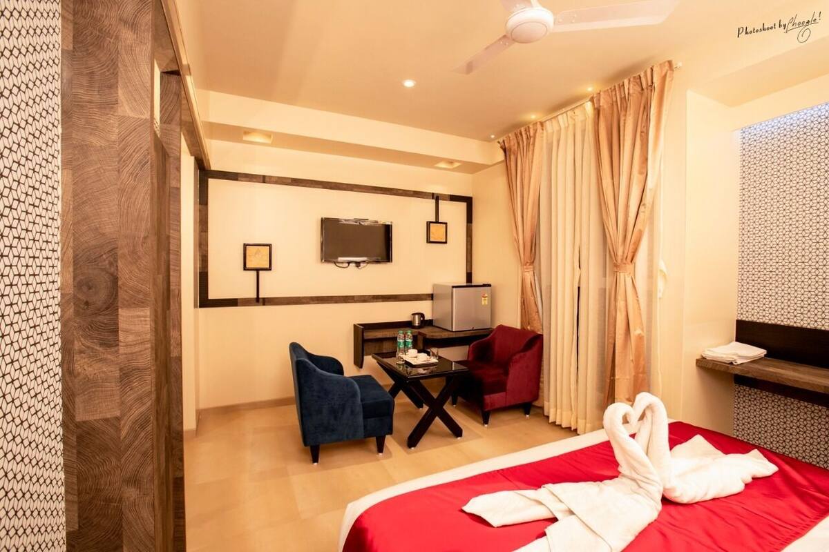 Quarto de hotel com uma cama, duas cadeiras, uma escrivaninha com televisão e um minibar.