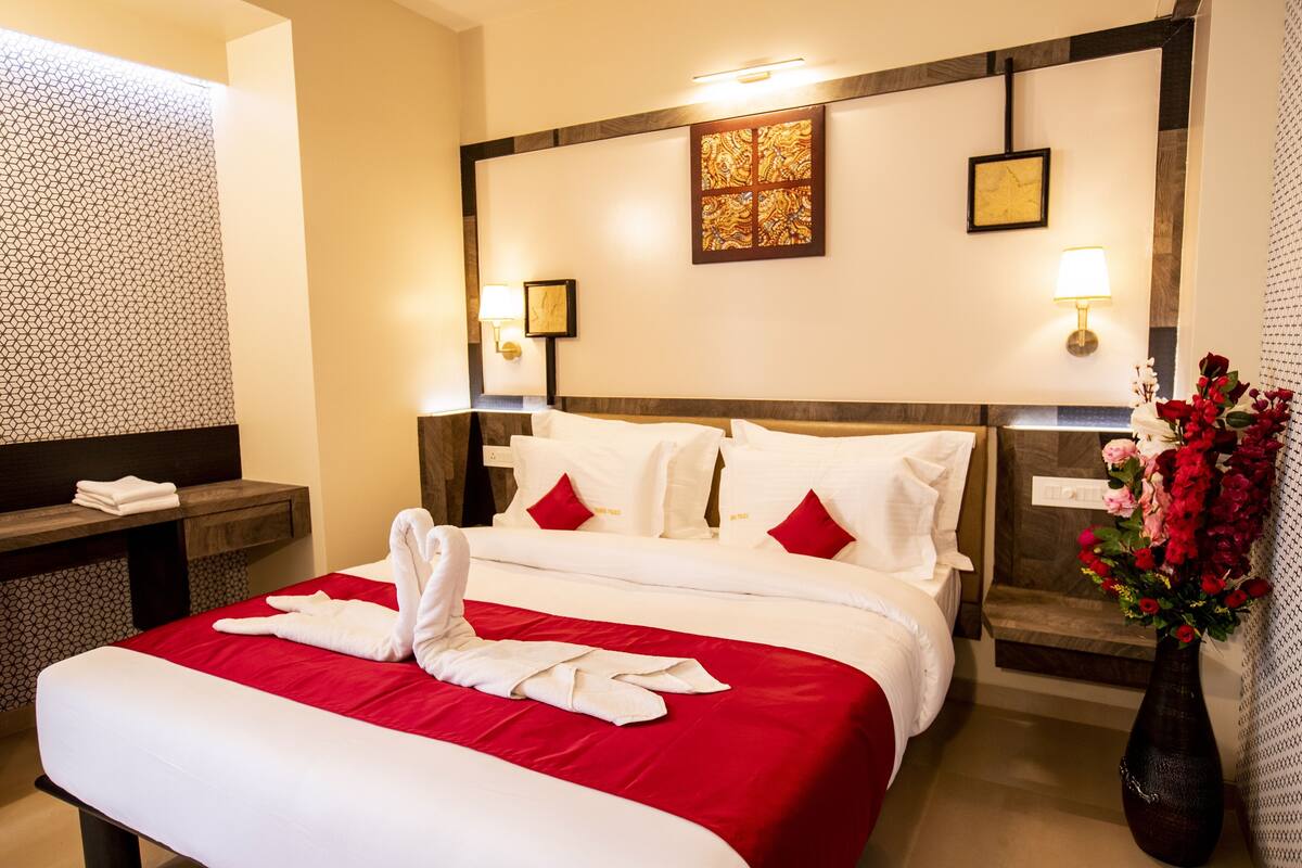 Quarto de hotel com uma cama grande, uma mesa de cabeceira, uma luminária na parede e uma obra de arte emoldurada acima da cama.