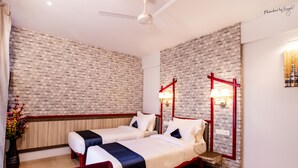 A hotel room with two beds, a red-framed nightstand, a vase with flowers, and a wall-mounted lamp. - Hotel Prabha Palace (Ahmednagar)