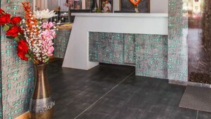 A reception area with a modern design, featuring a patterned wall, a white reception desk, and a framed portrait above it. - Hotel Prabha Palace (Ahmednagar)