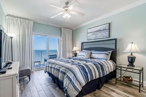 Une chambre avec un lit, un bureau, une chaise, un ventilateur de plafond, une table de chevet et une vue sur l’océan.