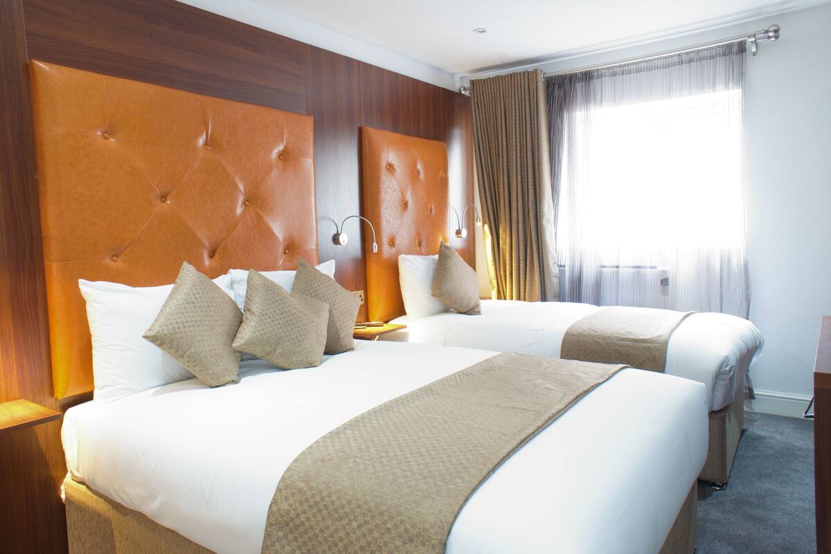A hotel room with two beds, each with a tufted headboard, white bedding, and beige throw blankets.