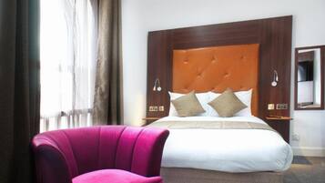A hotel room with a large bed, a wooden headboard, two bedside lamps, and a pink armchair.