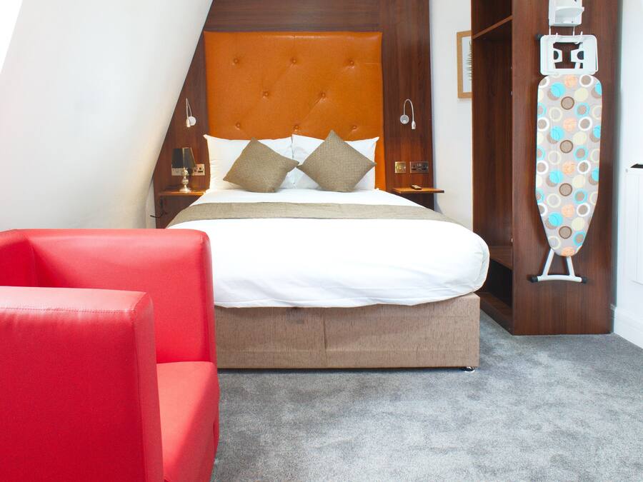 Un dormitorio con una cama, una silla roja y una tabla de planchar.