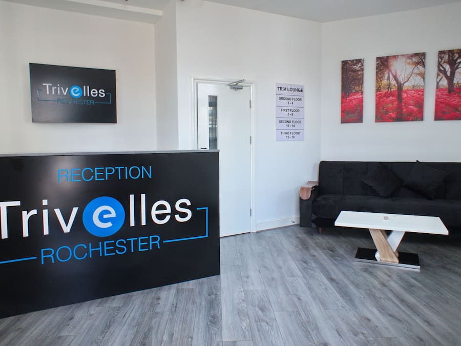 A reception area with a black reception desk labeled "Trivolles Rochester," a black sofa, and three red tree paintings on the wall.