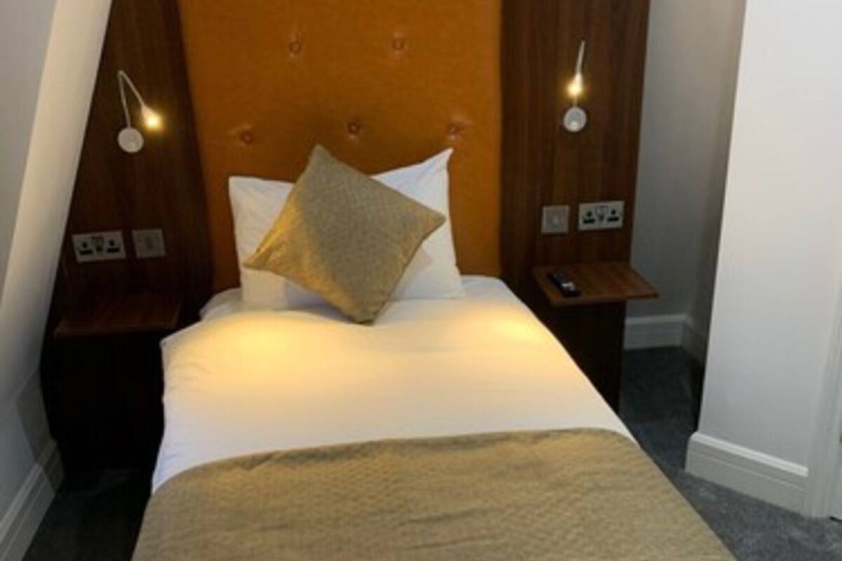 A hotel room with a large bed, wooden headboard, two bedside tables, and a nightstand.