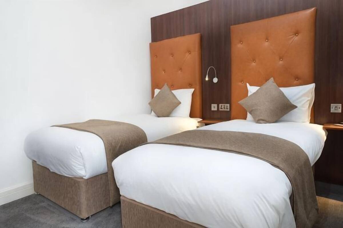 A hotel room with two beds, each with a headboard, white bedding, and a brown throw blanket.