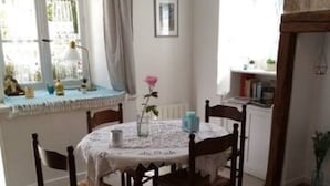 Et spiseområde med et rundt bord, fire stole, en vase med en enkelt blomst og et vindue med gardiner.