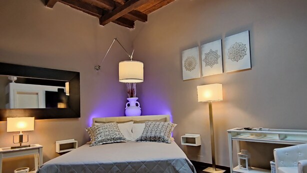 Ein Schlafzimmer mit Oberlicht, einem Bett mit gemusterten Kissen, Nachttischlampen, einem Nachttisch und einem Nachtschränkchen.