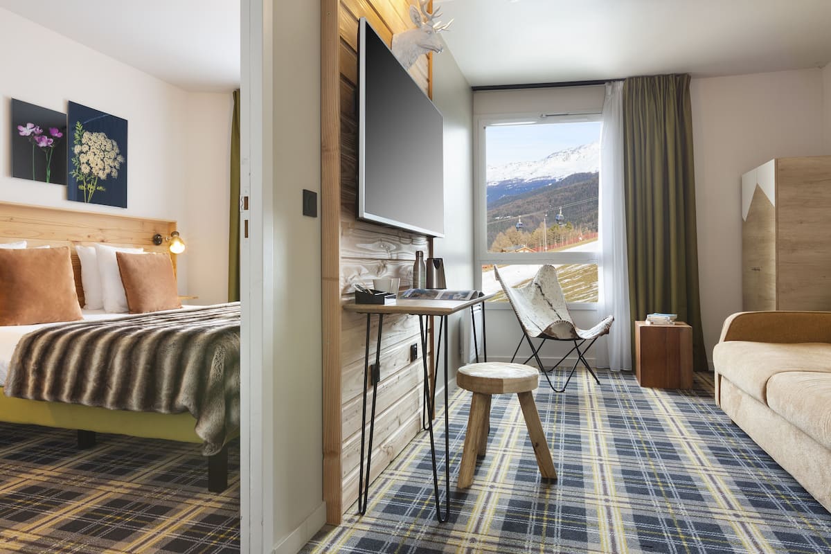 Habitación de hotel con cama, escritorio, silla y vista a las montañas.