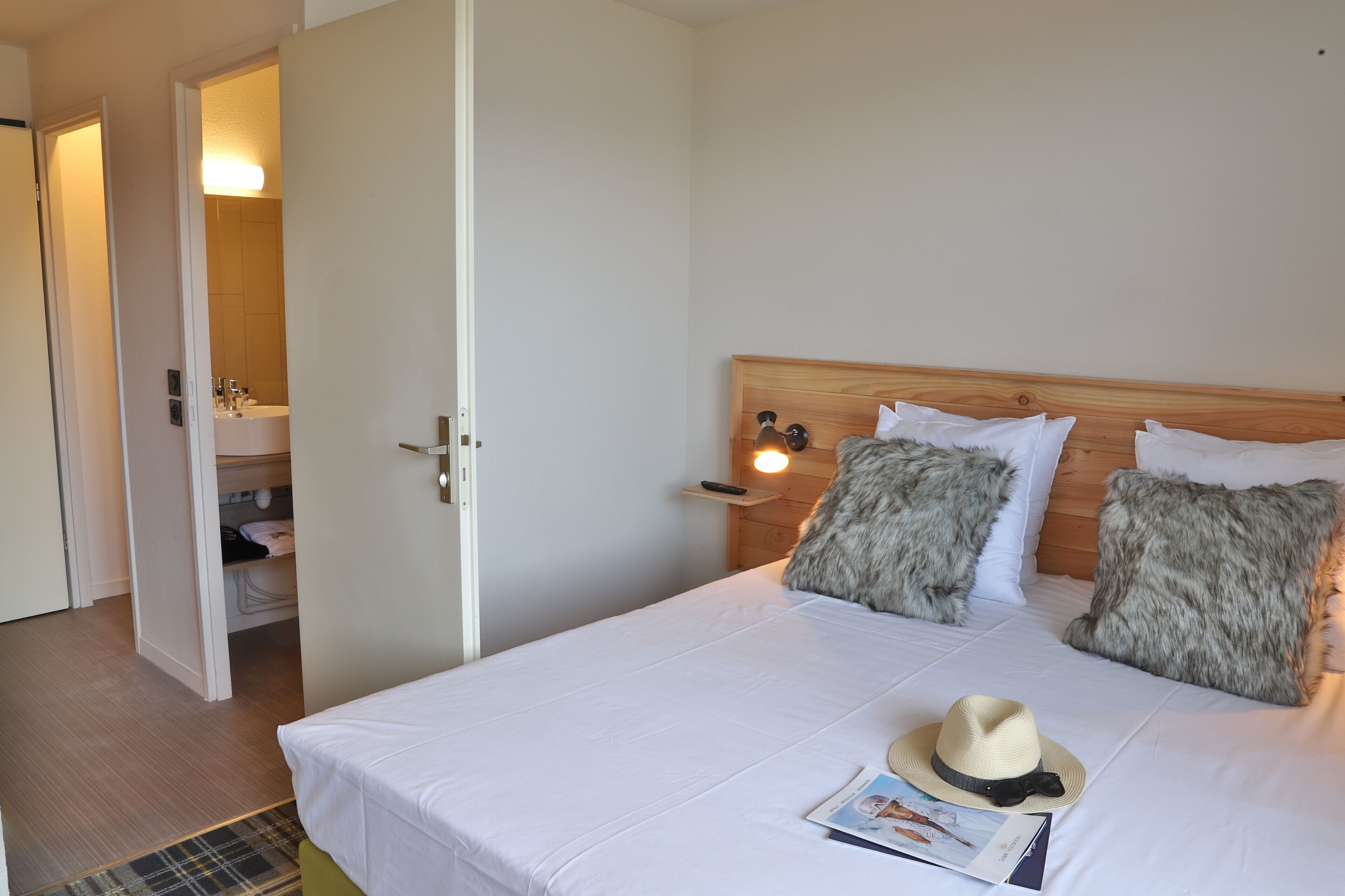 Een net opgemaakt bed met witte lakens, een hoed en een tijdschrift.