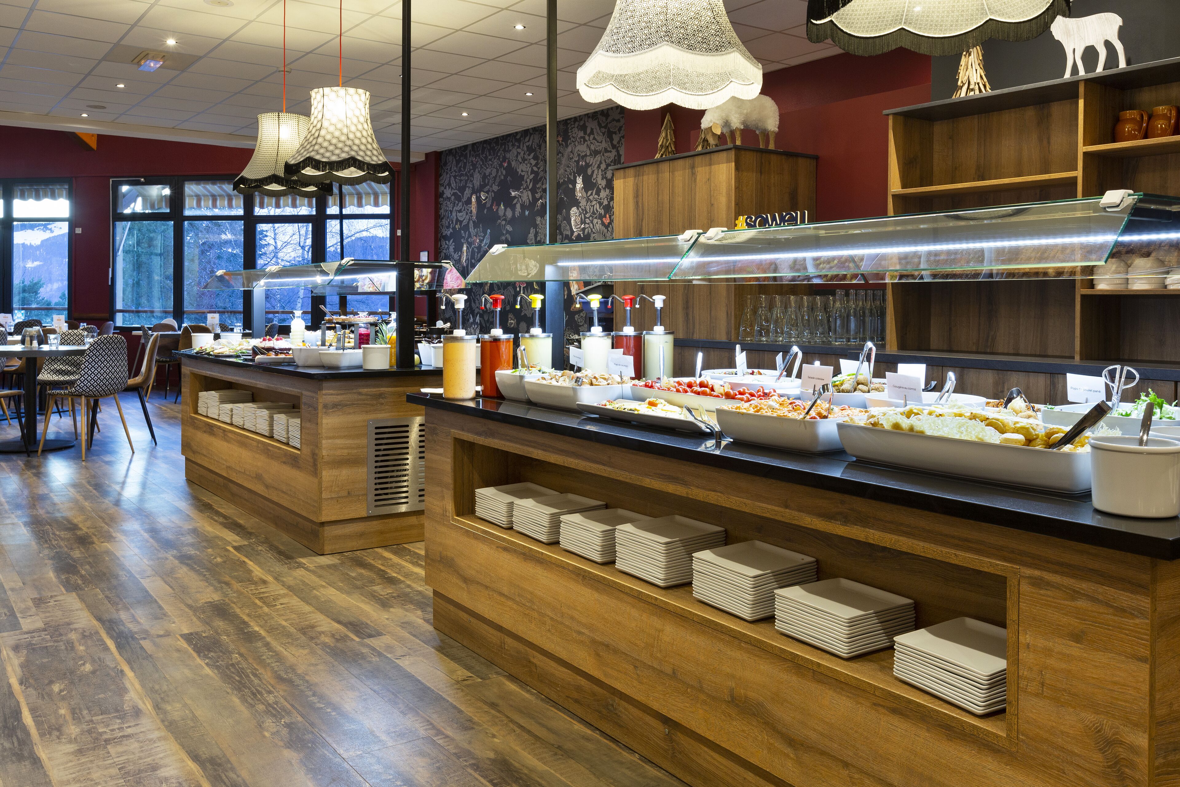 Een buffetgedeelte met verschillende food stations, houten toonbanken en uitzicht op de omgeving door grote ramen.