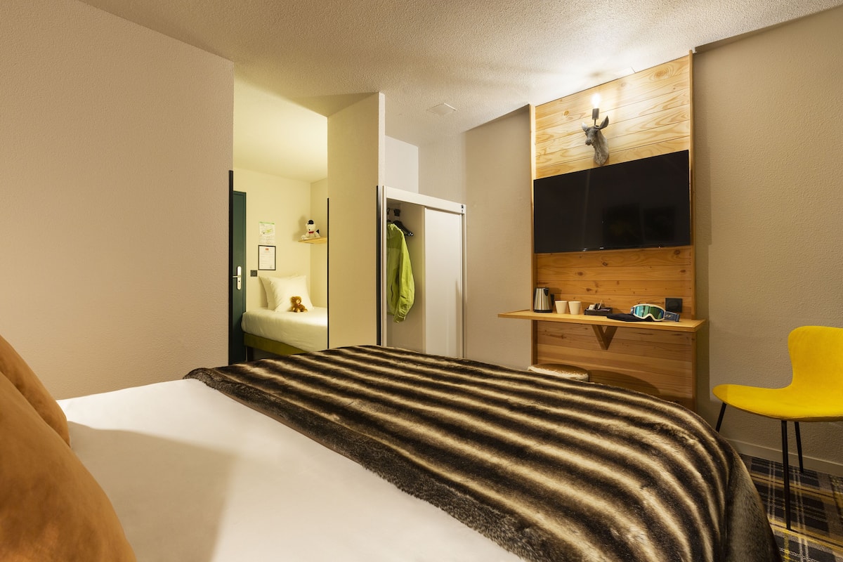 Una habitación de hotel con cama, escritorio, silla, televisión y baño visible a través de una puerta abierta.