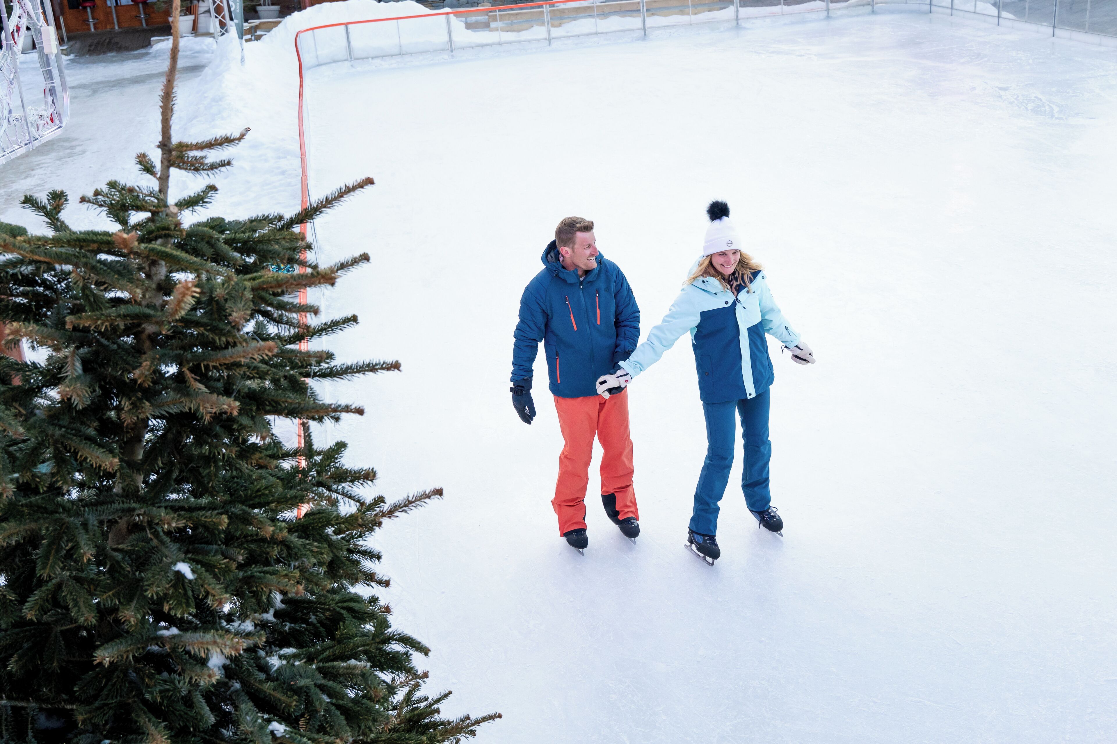 Two people ice skating on a rink with a Christmas tree in the foreground.