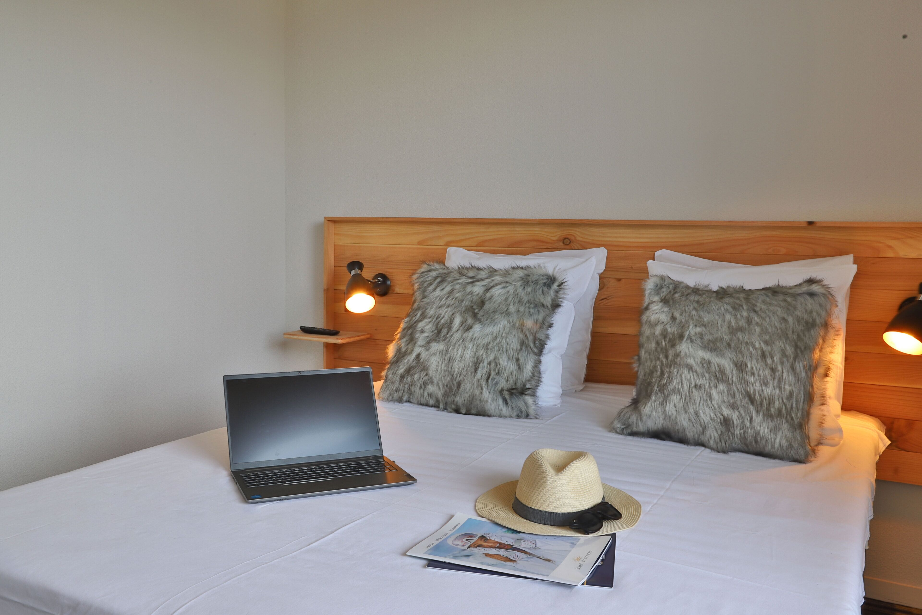 A bed with a laptop, a hat, and a magazine.