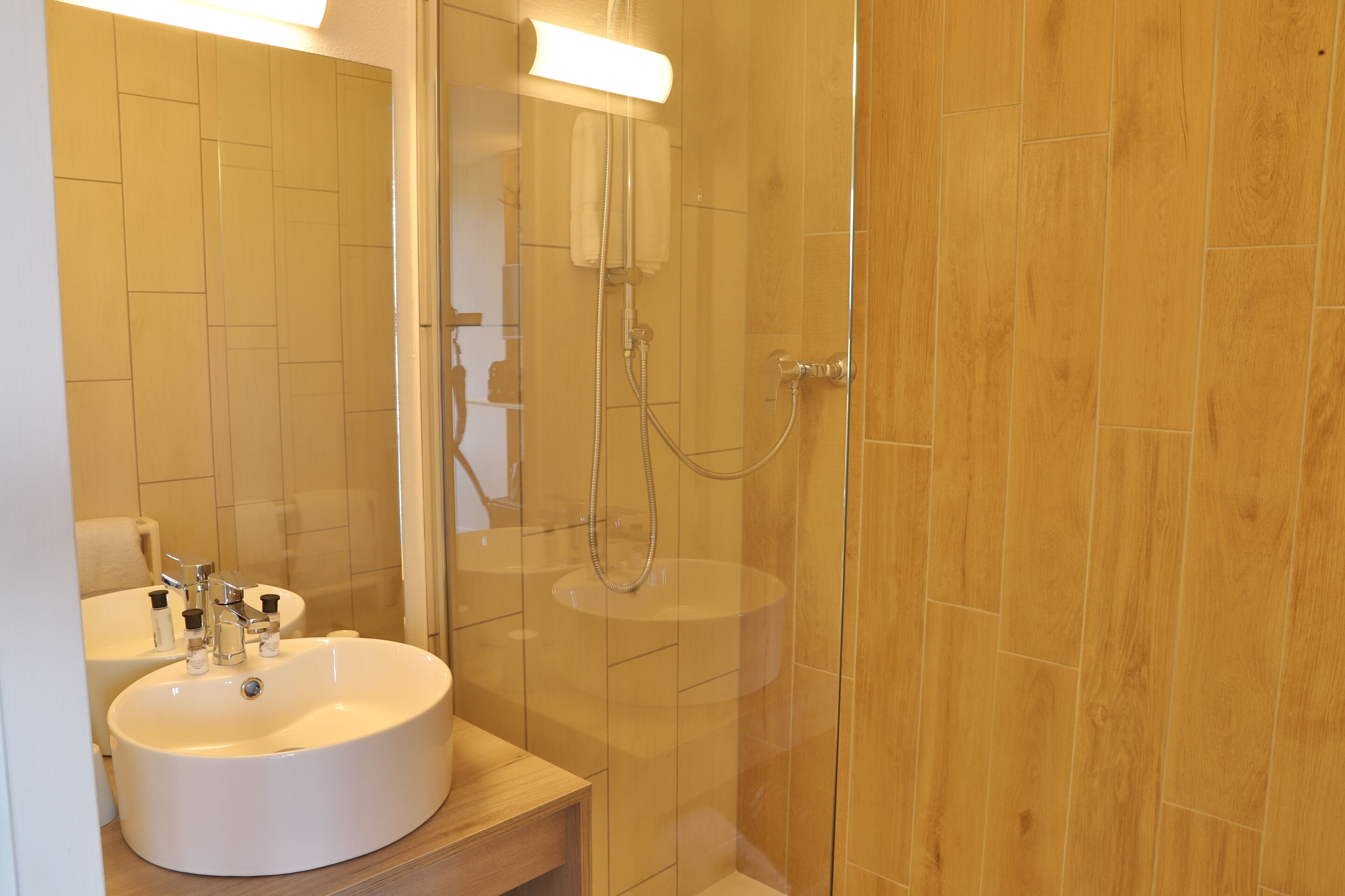 Ein Badezimmer mit einem großen, ovalen Waschbecken, einem Spiegel und einer Duschkabine.
