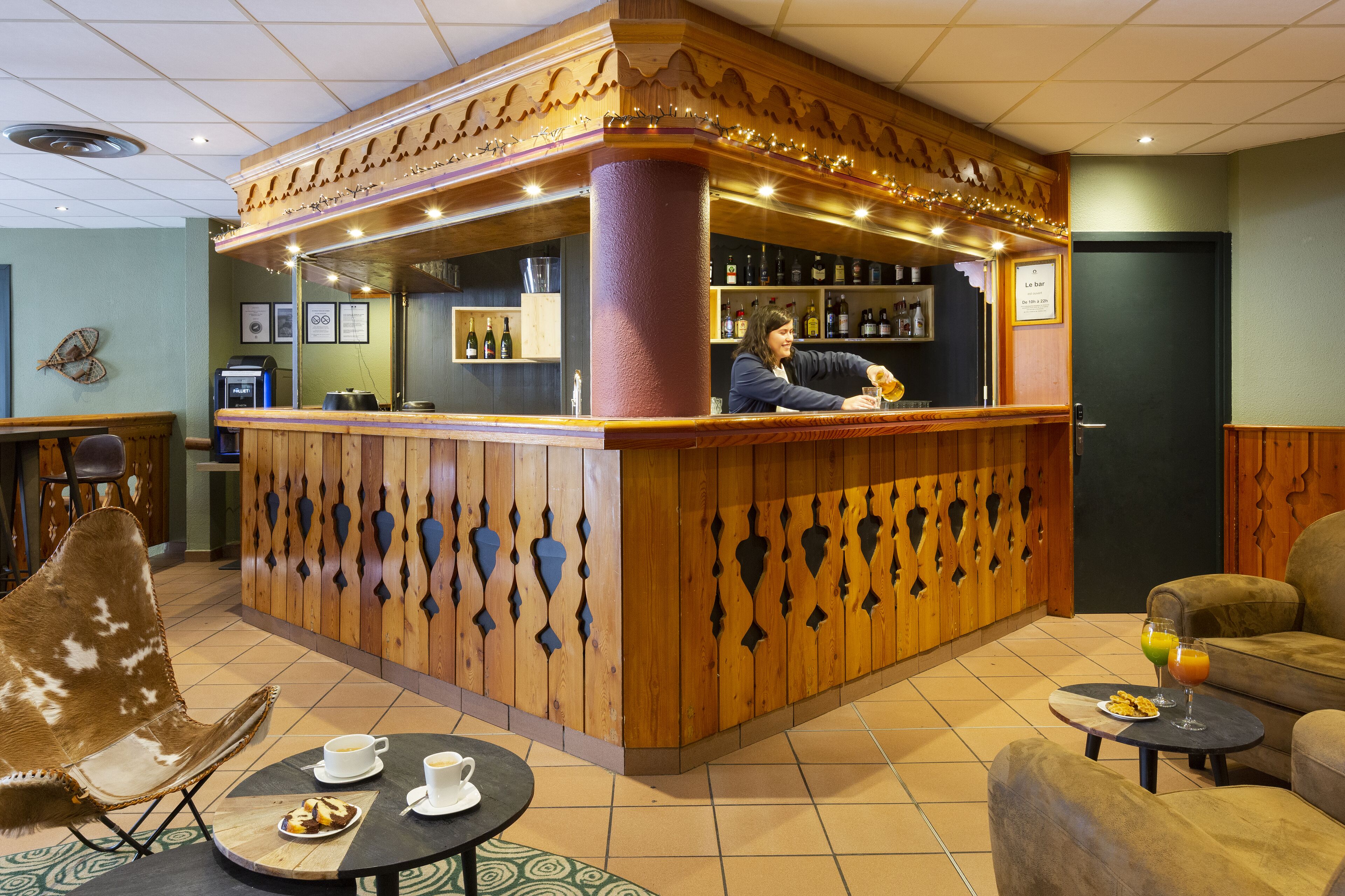 Un espace bar avec un comptoir en bois, des sièges comprenant un fauteuil en cuir, et une table sur laquelle se trouvent une assiette de nourriture et des boissons.