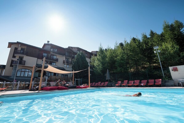 A swimming pool with red chairs and a building with balconies in the background.