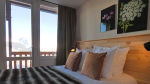 Un dormitorio con cama, almohadas, una manta, una mesita de noche, una lámpara y dos cuadros en la pared.