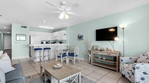 A modern living room with a dining area, kitchen, and a TV mounted on the wall. - Gulf Front, Stunning Views, Great Location + Free Attraction Tickets! (Seacrest)