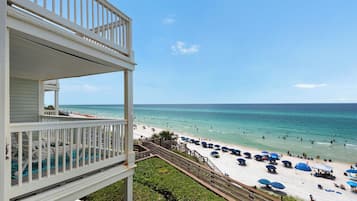 A beachfront property with a balcony overlooking the beach, a pool, and a clear view of the ocean.