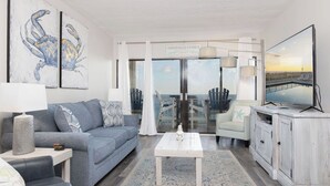 A modern living room with a grey sofa, a white coffee table, and a television on a cabinet. There are two framed artworks on the wall and a sign that reads "GONZALES FAMILY".