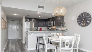 A modern kitchen with dark cabinets, a stainless steel refrigerator, and a white dining area with a round table and four chairs.