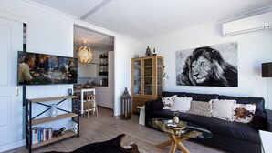 Sala de estar con un sofá negro, una mesa de centro de vidrio y un cuadro colgado con un león.