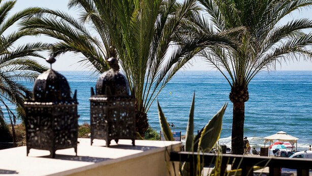 Terraza en la azotea con dos faroles decorativos, palmeras y vista al océano.