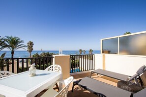 Un balcon avec une table blanche, deux chaises, un fauteuil et une vue sur la mer.