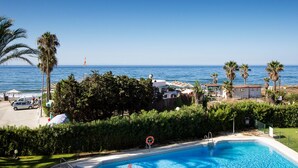 Una piscina con vistas al mar, rodeada de palmeras y un edificio de techo rojo.