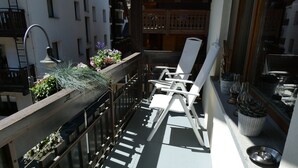 A balcony with a white chair, a small table, and potted plants. - Zermatt Rental Venus Topfloor Apartment.  (Zermatt)