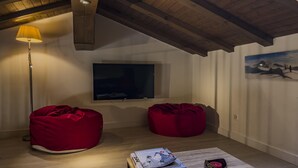 A cozy room with a wooden ceiling, a flat-screen TV mounted on the wall, two red bean bag chairs, a small table with a book and a candle, and a floor lamp. - Zermatt Rental Venus Topfloor Apartment.  (Zermatt)