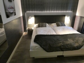 A modern hotel room with a large bed, two bedside tables, and a headboard with integrated lighting. - Zermatt Rental Venus Topfloor Apartment. (Zermatt)